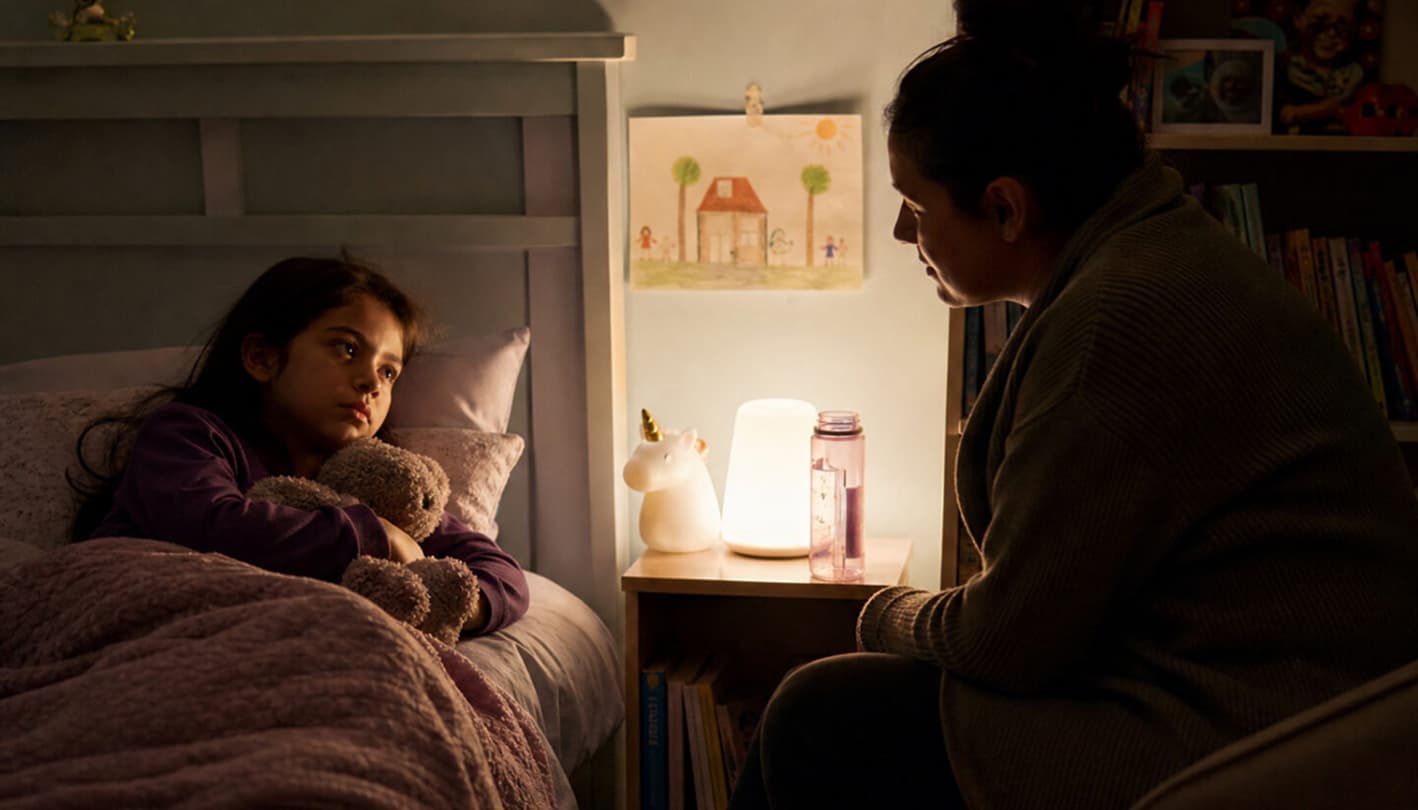 Pflegekind sitzt nachts verunsichert im Bett, Bezugsperson begleitet ruhig und unterstützend