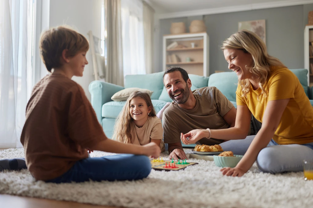 Eine Pflegefamilie spielt im Wohnzimmer mit dem eigenen und dem Pflegekind ein Brettspiel.